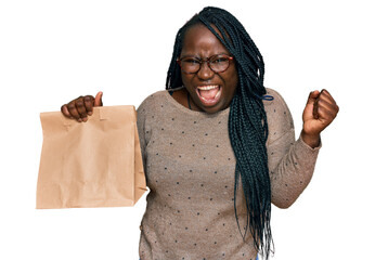 Wall Mural - Young black woman with braids holding take away paper bag screaming proud, celebrating victory and success very excited with raised arms