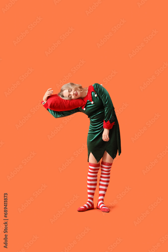 Sleepy young woman dressed as elf with pillow on orange background