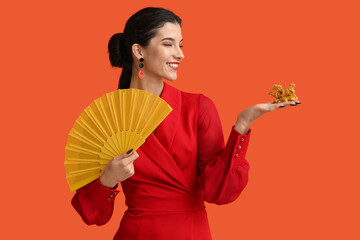 Poster - Beautiful young happy woman with golden dragon figurine and fan on orange background. Chinese New Year celebration