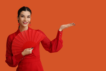 Poster - Beautiful young happy woman with fan pointing at something on orange background. Chinese New Year celebration