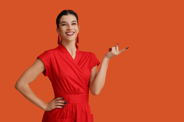 Poster - Beautiful young happy woman pointing at something on orange background. Chinese New Year celebration