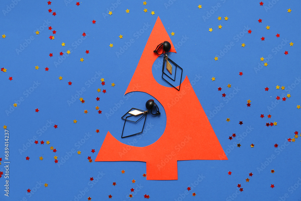 Paper Christmas tree with earrings and confetti on blue background
