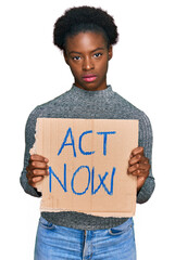 Canvas Print - Young african american girl holding act now banner thinking attitude and sober expression looking self confident