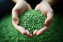 Close-up of hands holding a heap of green, eco-friendly biodegradable plastic pellets
