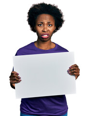 Sticker - African american woman with afro hair holding blank empty banner clueless and confused expression. doubt concept.