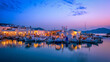 Picturesque panorama of Naousa town in famous tourist attraction Paros island, Greece with traditional whitewashed houses and moored fishing boats and seaside restaurants and cafe illuminated in night
