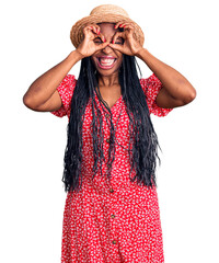 Canvas Print - Young african american woman wearing summer hat doing ok gesture like binoculars sticking tongue out, eyes looking through fingers. crazy expression.