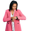 Beautiful hispanic woman wearing business jacket checking the time on wrist watch, relaxed and confident