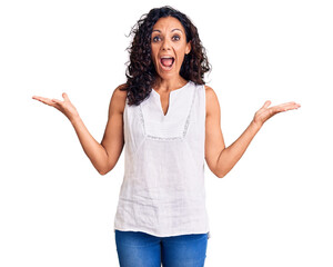 Wall Mural - Middle age beautiful woman wearing casual sleeveless t shirt celebrating victory with happy smile and winner expression with raised hands