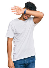 Wall Mural - Young arab man wearing casual white t shirt covering eyes with arm, looking serious and sad. sightless, hiding and rejection concept