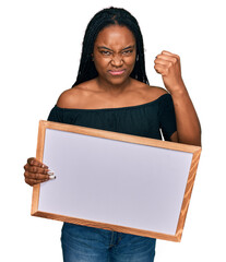 Poster - Young african american woman holding empty white chalkboard annoyed and frustrated shouting with anger, yelling crazy with anger and hand raised