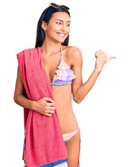 Poster - Young beautiful latin girl wearing bikini and sunglasses pointing thumb up to the side smiling happy with open mouth