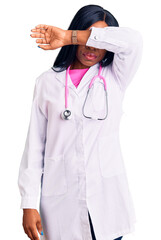 Sticker - Young african american woman wearing doctor stethoscope covering eyes with arm, looking serious and sad. sightless, hiding and rejection concept