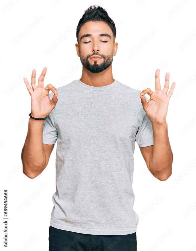Young man with beard wearing casual grey tshirt relax and smiling with eyes closed doing meditation gesture with fingers. yoga concept.