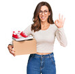 © Krakenimages.com - Young brunette woman holding box with red casual shoes doing ok sign with fingers, smiling friendly gesturing excellent symbol