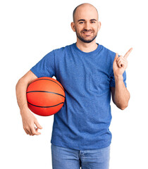 Wall Mural - Young handsome man holding basketball ball smiling happy pointing with hand and finger to the side