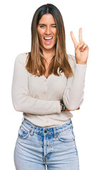 Wall Mural - Young woman wearing casual clothes smiling with happy face winking at the camera doing victory sign. number two.