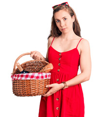 Poster - Young beautiful blonde woman holding picnic basket thinking attitude and sober expression looking self confident