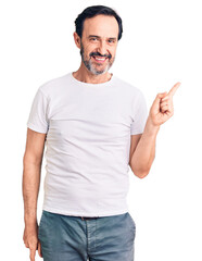 Wall Mural - Middle age handsome man wearing casual t-shirt with a big smile on face, pointing with hand finger to the side looking at the camera.