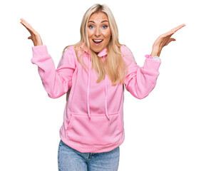 Wall Mural - Young blonde woman wearing casual sweatshirt celebrating crazy and amazed for success with arms raised and open eyes screaming excited. winner concept