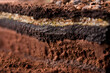 A cut cross-section side view of ground soil showing multiple layers of different types of earth composition underneath the topsoil. Ground surface dug out with layered soil formation below.