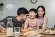 © pitipat - Asian Cute little boy eating vegetable salad with his parents in the kitchen. Lovely Asian family having breakfast together. Happy family activity lifestyle concept.
