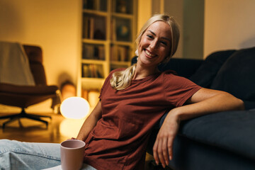 Wall Mural - Beautiful woman smiling at the camera and sitting on the floor at home.