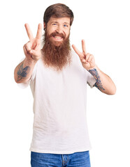 Canvas Print - Handsome young red head man with long beard wearing casual white tshirt smiling looking to the camera showing fingers doing victory sign. number two.