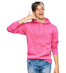 Canvas Print - Young hispanic man wearing casual pink sweatshirt smiling doing phone gesture with hand and fingers like talking on the telephone. communicating concepts.