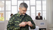 © Synthex🇺🇦 - Middle-aged soldier in military uniform attaching a vote pin at the polling station