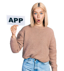 Poster - Beautiful young blonde woman holding app paper scared and amazed with open mouth for surprise, disbelief face