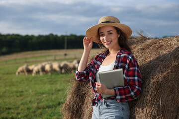 Wall Mural - Farmer with tablet near hay bale on farm. Space for text