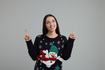 Sticker - Happy young woman in Christmas sweater pointing at something on grey background