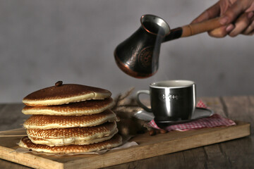 A close-up photo of a stack of five fluffy pancakes arranged on a wooden cutting board. The pancakes are golden brown and have a slightly crispy edge.