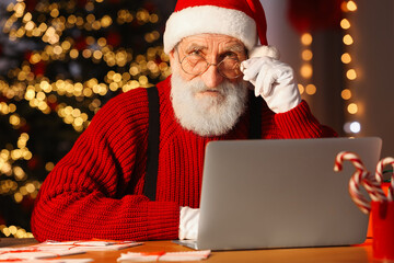 Poster - Santa Claus using laptop at his workplace in room decorated for Christmas