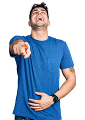 Wall Mural - Young hispanic man wearing casual t shirt laughing at you, pointing finger to the camera with hand over body, shame expression