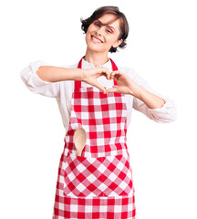 Poster - Beautiful young woman with short hair wearing professional cook apron smiling in love doing heart symbol shape with hands. romantic concept.