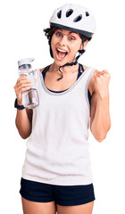 Poster - Beautiful young woman with short hair wearing bike helmet and holding water bottle screaming proud, celebrating victory and success very excited with raised arms