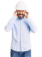 Canvas Print - Young handsome man wearing architect hardhat covering ears with fingers with annoyed expression for the noise of loud music. deaf concept.