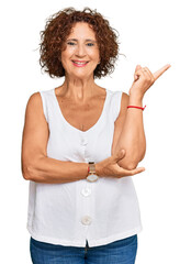 Wall Mural - Beautiful middle age mature woman wearing casual white shirt with a big smile on face, pointing with hand and finger to the side looking at the camera.