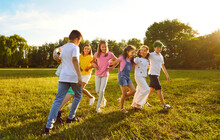 Group Of A Playful Kids Friends Playing Active Outdoor Games On A Green Grass In The Summer Park. Happy Children Having Fun Outside On A Sunny Day In The Camp. Summer Holiday Concept.