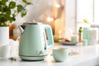 Electric green kettle and tea or coffee cups on the table in a modern kitchen in light colors. Modern Tea set for quick preparation of hot drinks.