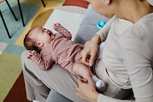 Top Down Shot Of Crying Baby Dressed In Pastel Bodysuit Lying On Mom Lap, Copy Space