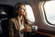 Smiling businesswoman holding a cup of coffee and looking out the airplane window. Businesswoman looking out window of private jet. Happy flight and airplane travel concept.