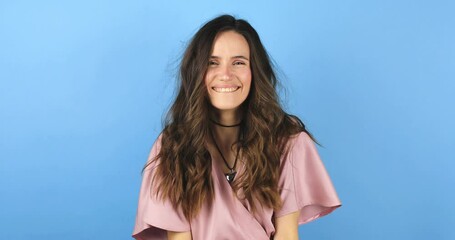 Wall Mural - Lovely coquettish brunette curly woman, winking playfully, flirting. Woman wear pink dress fix her hair on blue background. Lovely coquettish brunette woman, playfully flirting.