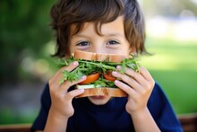 a child eating a humongous sandwich with fresh herbs