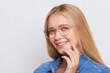© South House Studio - Fair-haired girl closeup wears blue denim shirt and glasses holds one hand at her face and smiles, good mood concept, copy space