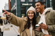 © Drobot Dean - Cheerful couple pointing away while drinking coffee standing at street