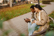 Smiling couple drinking coffee and using smartphones while spending time together in park