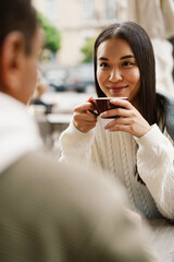 Canvas Print - Smiling woman drinking coffee while spending time in cafe with young man